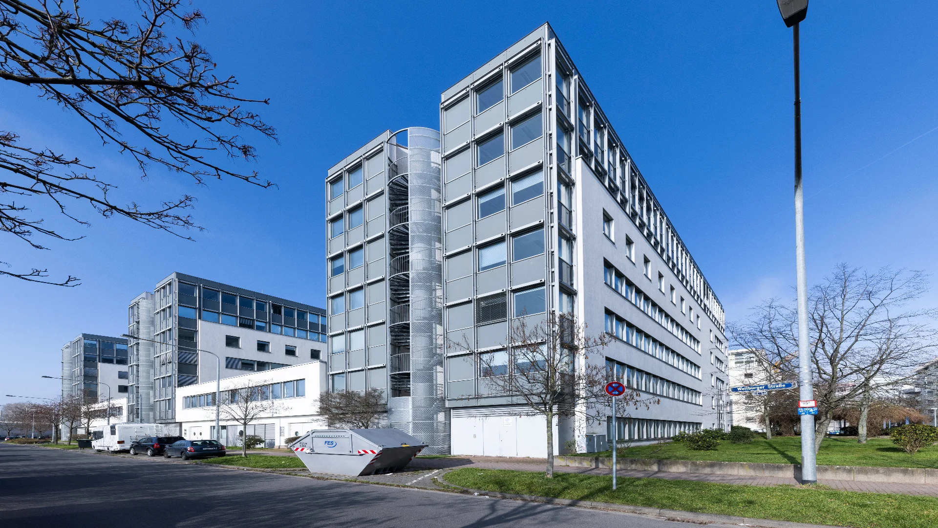 Mehrgeschossige Bürogebäude mit heller Metallfassade und rundem Glastreppenturm im Gewerbepark